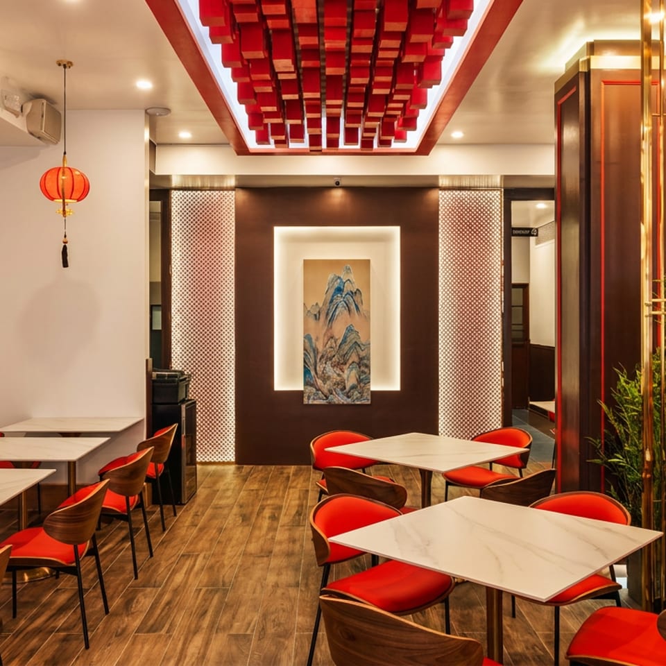 Elegant Chinese restaurant dining room with red lanterns, red chairs, marble tables, wood flooring, and mountain artwork.