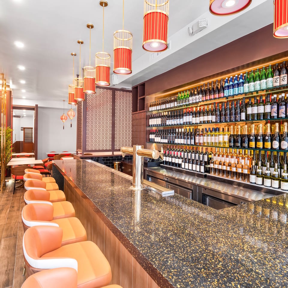 A modern restaurant bar with orange stools, a speckled countertop, and shelves of liquor bottles.