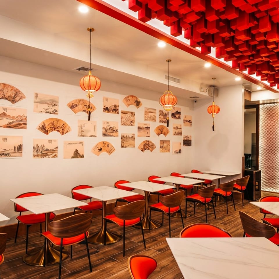 Modern restaurant interior with red chairs, white tables, Asian art on walls, and red lantern lighting.