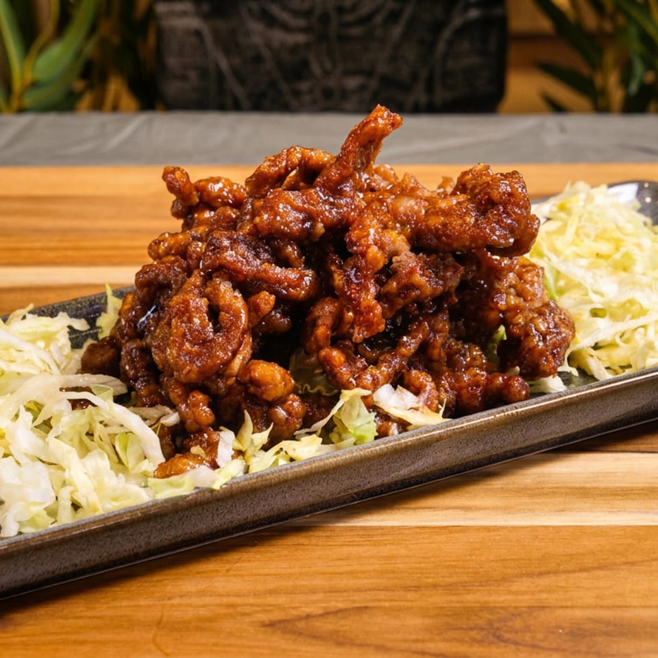 Crispy, sauce-coated fried chicken served over shredded cabbage on a black rectangular plate atop a wooden table.