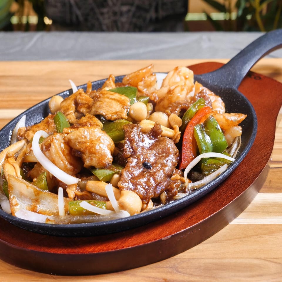Sizzling platter of beef, chicken, shrimp, and vegetables on a wooden table.